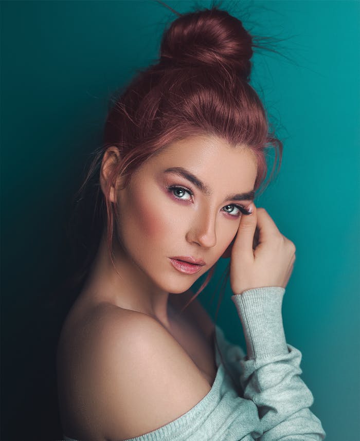 A fashionable adult woman posing with elegant makeup against a teal background.